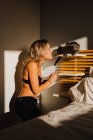Без сорочки жінка приборкає милий кіт в полиці спальні біля ліжка зі світлом, що потрапляє в кімнату — стокове фото
