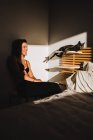 Блестящая женщина рядом с симпатичной кошкой в тени спальни, рядом кровать с проникающим в комнату светом — стоковое фото