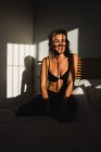Съемка чувственной красивой женщины улыбаясь между светом и тенями в нижнем белье на кровати глядя в сторону — стоковое фото