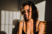 Shooting einer sinnlichen hübschen Frau, die zwischen Licht und Schatten in Dessous auf dem Bett lächelt und wegschaut — Stockfoto