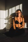 Tiro de uma mulher bonita sensual sorrindo entre a luz e as sombras em lingerie na cama olhando para a câmera — Fotografia de Stock