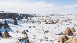 Сверху все тело неузнаваемой пары туристов, стоящих на камне и любующихся удивительными снежными пейзажами на безоблачном голубом небе над снежным горным ландшафтом в солнечный зимний день в Каппадокии, Турция — стоковое фото