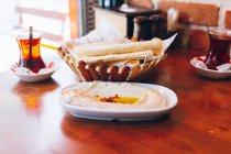 Piatto di delizioso hummus con olio e spezie posto sul tavolo vicino a pane piatto e tè caldo nel caffè tradizionale in Turchia — Foto stock