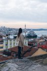 Vista posteriore della donna alla moda in piedi sul bordo squallido roccia contro quartiere residenziale e cielo nuvoloso tramonto la sera in Turchia — Foto stock