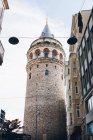 From below aged Galata Tower located near residential building against cloudy sky on street of Istanbul, Turkey — Stock Photo