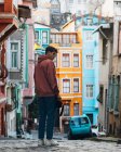 Back view of young man with photo camera standing on paved road near colorful houses and blue car on city street in Turkey — Stock Photo