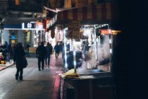Cocinero irreconocible preparando platos tradicionales para vender en establo contra la calle con gente caminando en iluminación por la noche en la ciudad de Turquía - foto de stock