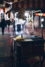 Unbekannter Koch bereitet traditionelle Gerichte für den Verkauf in einem Verkaufsstand gegen Straße mit Menschen, die nachts in der Stadt der Türkei in Illumination laufen — Stockfoto