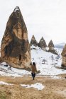Rückansicht einer nicht wiedererkennbaren Frau, die auf einem Feldweg gegen einen schneebedeckten Hügel mit berühmten Säulen mit scharfen, speerförmigen Gipfeln im Nationalpark in der Türkei geht — Stockfoto