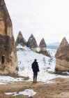 Back view of man in dark warm clothes looking away while standing on dirt road against snowy hill with famous pillars with sharp spear shaped peaks in national park in Turkey — Stock Photo