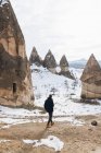 Назад погляд людини в темному теплому одязі, що дивиться в далечінь, стоячи на брудній дорозі проти снігового пагорба з відомими стовпами з гострими вершинами у вигляді списа в національному парку в Туреччині. — стокове фото