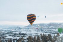 Multicolored air balloons n cloudy sky over ancient settlement with stone and cave houses against foggy highland in overcast weather in Turkey — Stock Photo