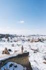 Du haut du corps entier, une touriste féminine méconnaissable debout sur la pierre et admirant une vue imprenable sur un ciel bleu sans nuages sur un terrain montagneux enneigé par une journée ensoleillée d'hiver en Cappadoce, Turquie — Photo de stock