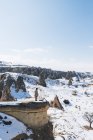 Du haut du corps entier, une touriste féminine méconnaissable debout sur la pierre et admirant une vue imprenable sur un ciel bleu sans nuages sur un terrain montagneux enneigé par une journée ensoleillée d'hiver en Cappadoce, Turquie — Photo de stock