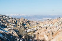 Von oben Gelände mit berühmten Siedlungen mit alten Steinhäusern in Höhlen, die wie Feenhäuser im Mönchtal vor verschneiten Bergen am Horizont unter blauem Himmel in der Türkei stehen — Stockfoto