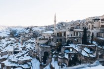 Над маленьким містечком з давніми будівлями в долині і високою вежею мінарету на сніжному схилі гори проти безхмарного блакитного неба взимку в Туреччині. — стокове фото