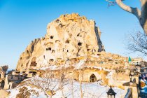 Низкий угол старинного замка, высеченного в скале и покрытого белым снегом против безоблачного неба на улице поселка Учисар в Каппадокии, Турция — стоковое фото