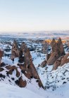 Vue aérienne d'un homme méconnaissable debout sur des formations rocheuses rugueuses recouvertes de neige blanche contre un ciel nocturne sans nuages en Cappadoce, Turquie — Photo de stock