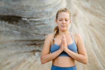 Junge achtsame Frau in Sportkleidung meditiert mit geschlossenen Augen, während sie Yoga auf verschwommenem Hintergrund praktiziert — Stockfoto