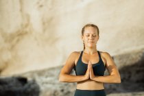 Молодая внимательная женщина в спортивной одежде медитирует с закрытыми глазами, практикуя йогу на размытом фоне — стоковое фото
