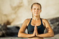 Jovem mindful fêmea em sportswear meditando olhando para a câmera enquanto pratica ioga no fundo borrado — Fotografia de Stock