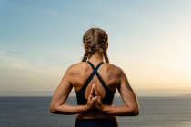 Back view of anonymous female with namaste hands practicing yoga against ocean in twilight in back lit — Stock Photo