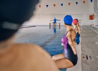 Gruppe von Menschen in Badebekleidung, die am Pool sitzen und die erhobenen Arme ausstrecken, während sie während des Wassergymnastik-Trainings mit dem Trainer im Pool trainieren — Stockfoto