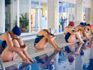 Grupo de pessoas em trajes de banho sentado à beira da piscina e alongamento braços levantados durante o exercício durante o treinamento de aeróbica aquática com instrutor na piscina — Fotografia de Stock