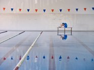 Vista lateral do corpo de alongamento treinador e abraçando os joelhos enquanto faz exercício durante o treinamento de aeróbica aquática na piscina — Fotografia de Stock