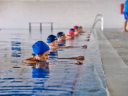 Groupe de personnes en bonnet de bain debout dans la piscine pendant le cours d'aérobic aquatique — Photo de stock
