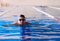 Varón de mediana edad en gafas y gorra nadando en piscina durante aeróbic acuático - foto de stock