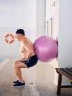 Vue latérale du nageur masculin d'âge moyen faisant des exercices de squat avec ballon de remise en forme pendant l'entraînement d'aérobic dans la piscine — Photo de stock