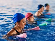 Vue latérale du groupe de personnes en maillots de bain pratiquant avec des nouilles en mousse aqua dans la piscine pendant l'aérobic aquatique — Photo de stock