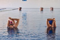 Empresa de personas anónimas en traje de baño estirando los brazos en la piscina mientras hace ejercicio durante el entrenamiento aeróbico acuático - foto de stock