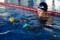 Фокусована зріла жінка плаває вправами з гантелями в басейні під час тренування водної аеробіки — стокове фото