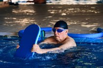 Middle aged male swimming with foam board while training during water aerobics in pool — Stock Photo