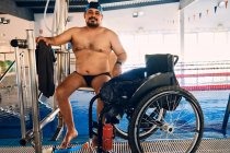 Зрелый мужчина, сидящий на стуле бассейна подъемник возле инвалидной коляски перед тренировкой — стоковое фото
