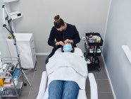 Von oben von professionellen Kosmetikerin Anwendung Reinigungsmittel auf Wimpern der weiblichen Klientin während der Schönheitsbehandlung im Salon — Stockfoto
