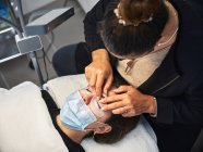 From above crop anonymous beauty master applying lash lift shield on eyelid of female client during eyelash treatment in salon — Stock Photo