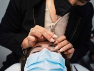 Closeup of crop anonymous cosmetician with applicator covering eyelashes of woman with solution for lash lifting during beauty procedure in salon — Stock Photo