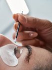 Nahaufnahme einer anonymen Kosmetikerin mit Applikator, die die Augenbraue einer Kundin mit Vergangenheit für die Laminierung während der Schönheitsbehandlung im Salon bedeckt — Stockfoto