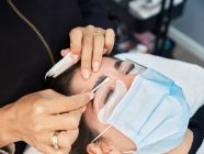 Closeup of crop anonymous beautician with applicator covering eyebrow of female client with past for lamination during beauty treatment in salon — Stock Photo