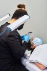Профессиональный косметолог со смартфоном фотографирует лицо клиентки, получающей лечение ресниц во время процедуры красоты в салоне — стоковое фото