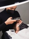 From above of professional cosmetologist with mobile phone shooting process of eyelash extension procedure in beauty salon with ring light — Stock Photo