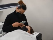 Профессиональный косметолог с процессом съемки мобильных телефонов процедуры наращивания ресниц в салоне красоты с кольцевым светом — стоковое фото