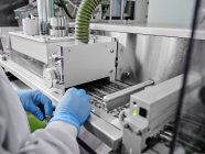Crop unrecognizable factory worker in gloves working at automatic conveyor with capsule pills in blisters at pharmaceutical manufacturing plant — Stock Photo