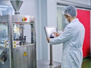 Vue latérale du chimiste masculin dans une machine de remplissage de capsules à fonctionnement uniforme à l'usine de fabrication pharmaceutique — Photo de stock