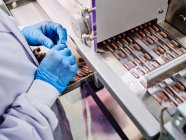 Erntehelfer in Handschuhen, die am automatischen Förderband mit Kapselpillen in Blistern in pharmazeutischer Produktionsanlage arbeiten — Stockfoto