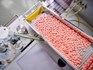 Сучасна фармацевтична машина з купою рожевих таблеток на конвеєрі, розміщеному у виробничій лабораторії — стокове фото