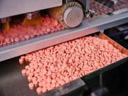 Современная фармацевтическая машина с грудами розовых таблеток на конвейере размещена в производственной лаборатории — стоковое фото